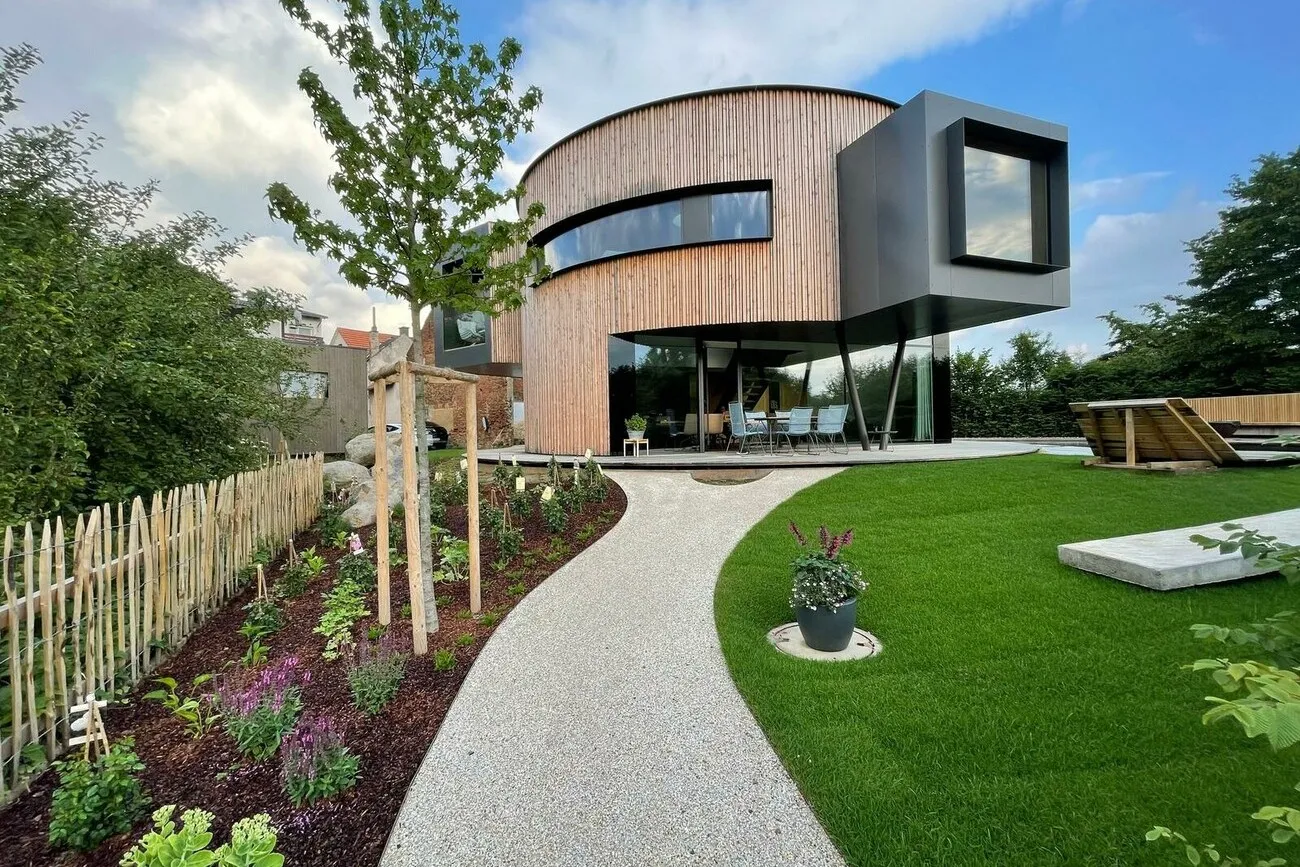 Das Drehhaus mit einer Holzoptik aus der Gartenansicht mit Blick auf den freischwebenden Teil des Drehhauses einen grauen Weg und grünen Garten.