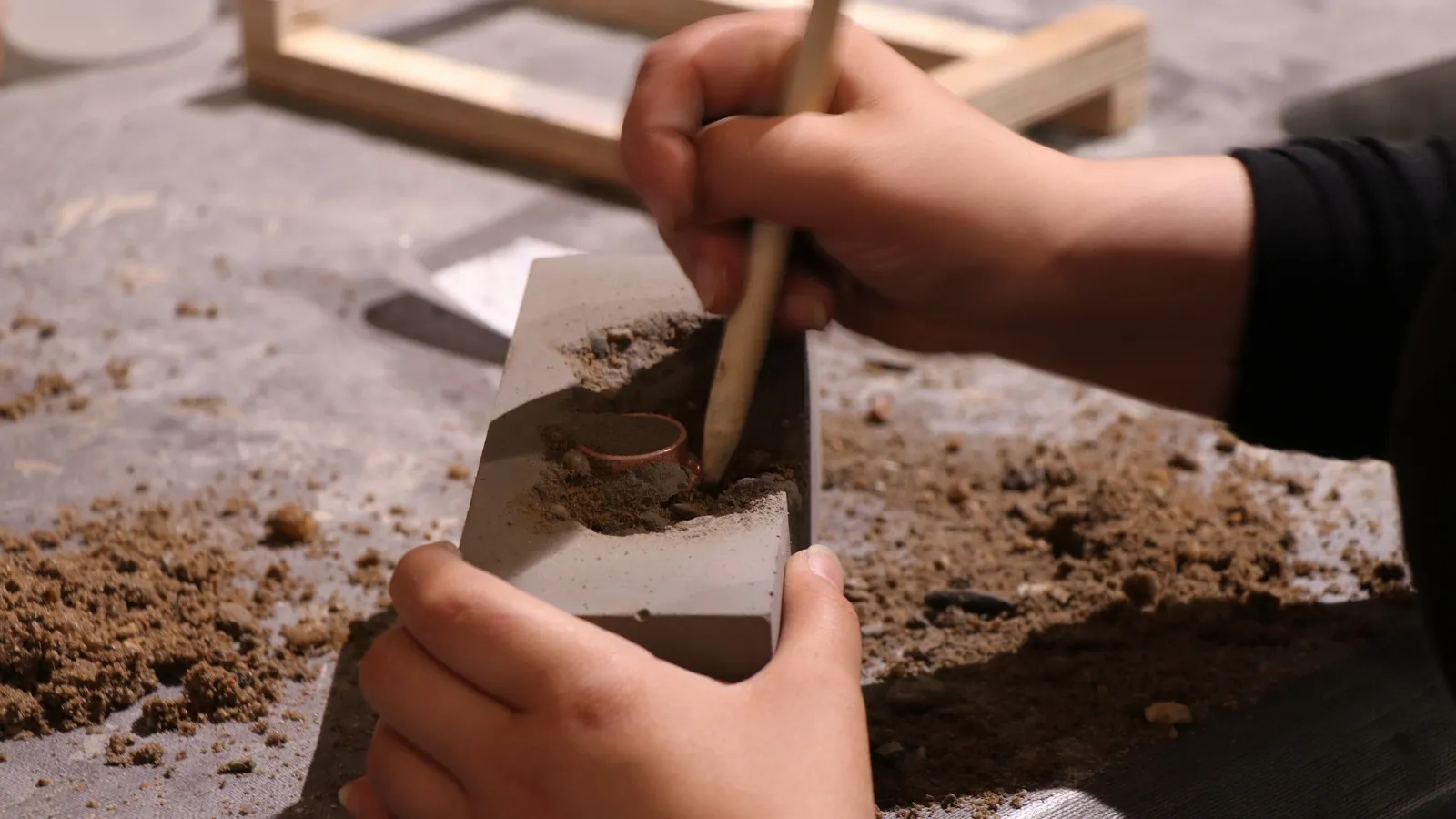 Eine Schülerin kratzt mit der Pinselrückseite Kies aus dem ausgehärteten Beton.