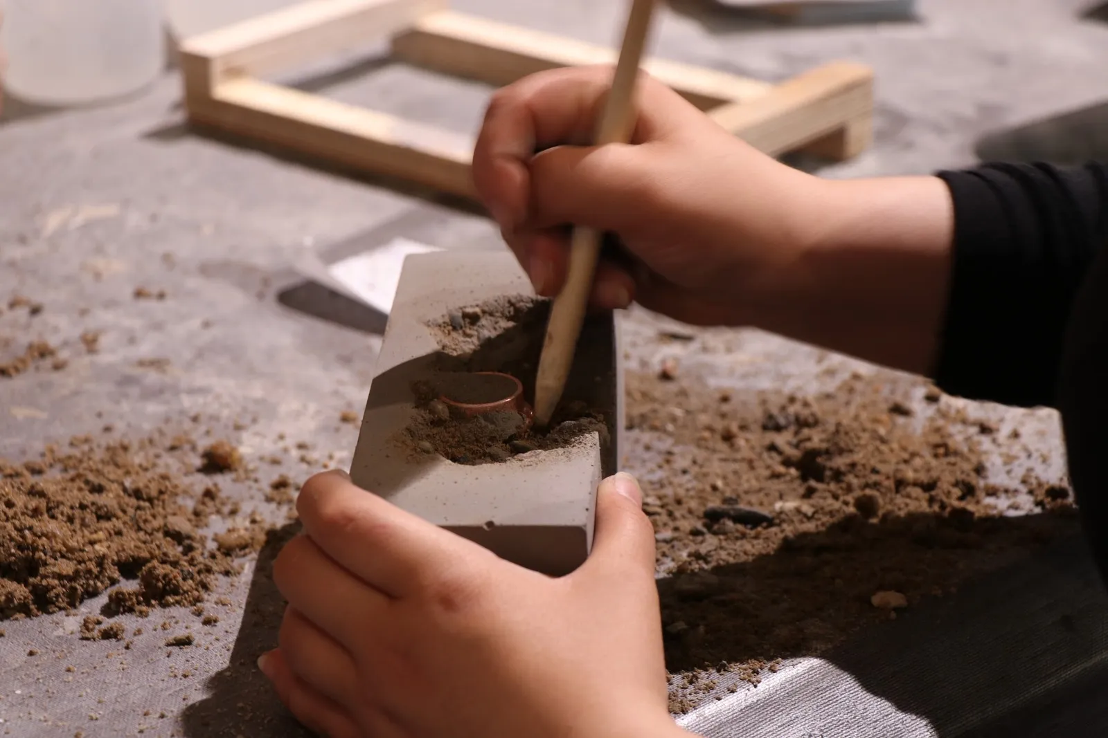 Eine Schülerin kratzt mit der Pinselrückseite Kies aus dem ausgehärteten Beton.