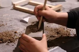Eine Schülerin kratzt mit der Pinselrückseite Kies aus dem ausgehärteten Beton.