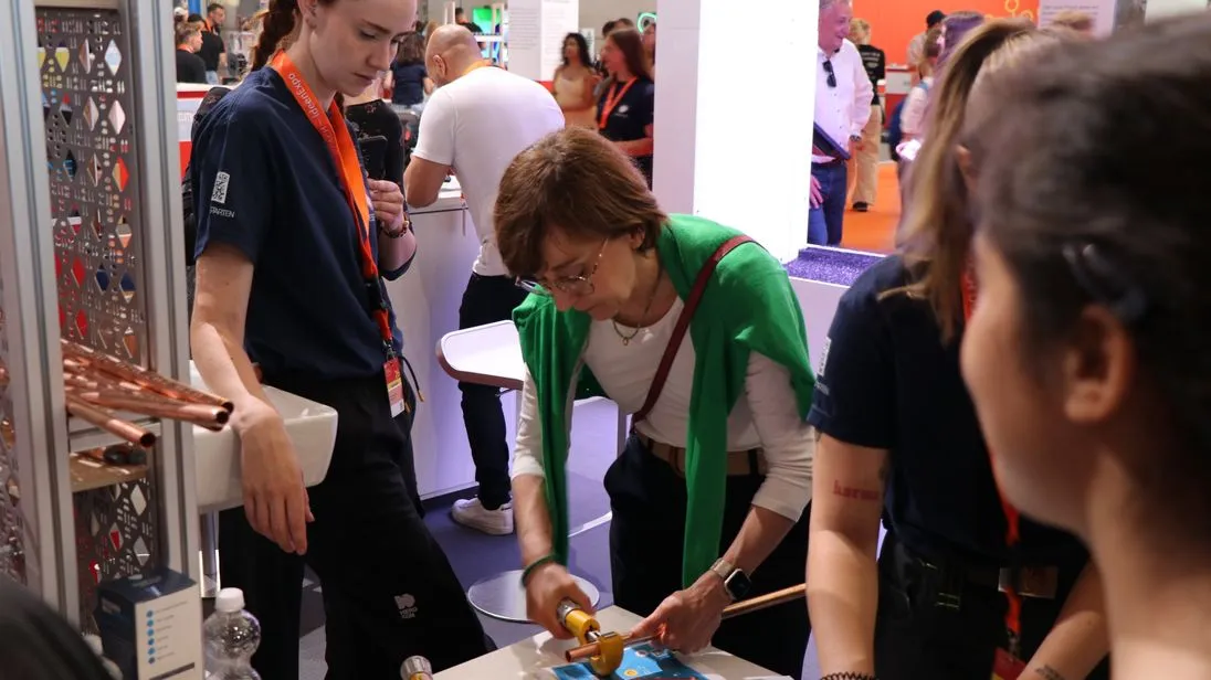 Sandra Hunke, Content Creatorin und gelernte Anlagenmechanikerin im Bereich Sanitär, Heizung und Klima, unterstützt Staatssekretärin Christine Arbogast beim Ablängen eines Kupferrohrs.