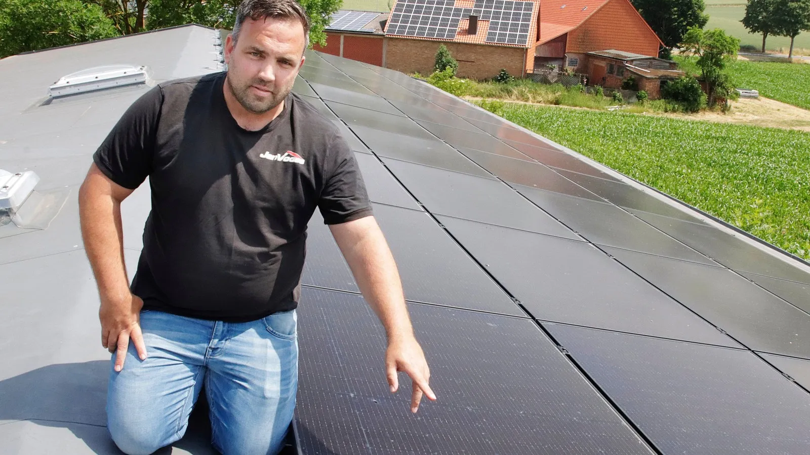 Foto von Dachdeckermeister Jan Voges, der auf dem Dach eines Hauses auf Photovoltaikplatten kniet.