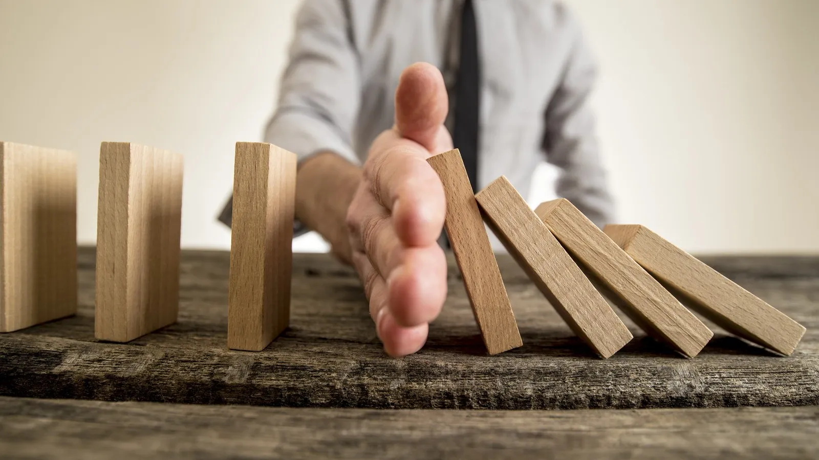 Businessman halting the domino effect inserting his hand between falling and upright wooden blocks in a close up conceptual image.