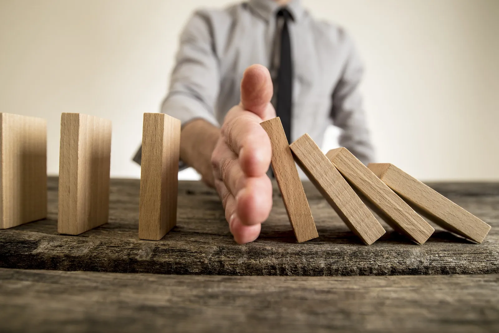 Businessman halting the domino effect inserting his hand between falling and upright wooden blocks in a close up conceptual image.