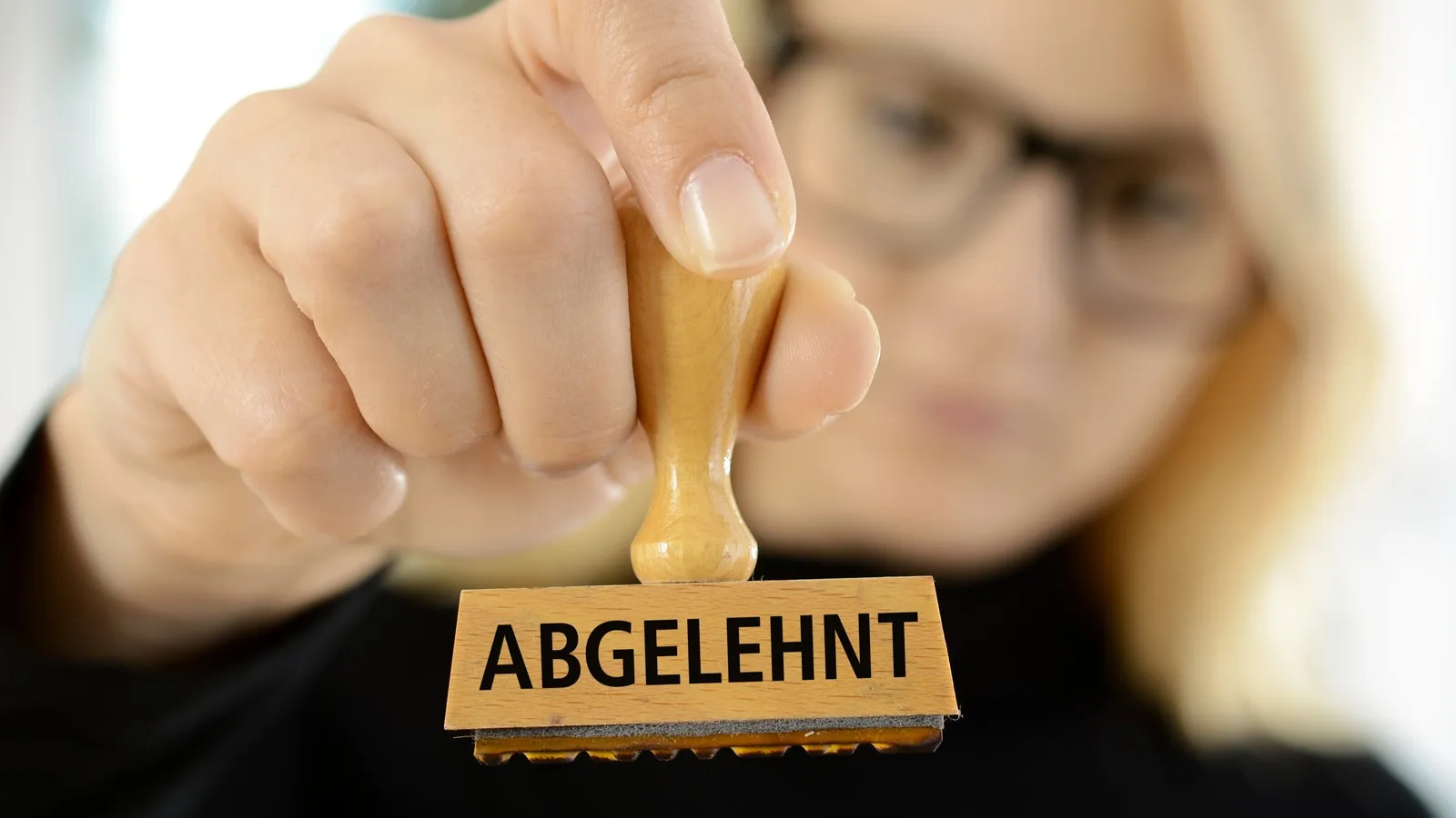 Eine Frau hält einen Stempel mit der Aufschrift "abgelehnt" in der Hand.