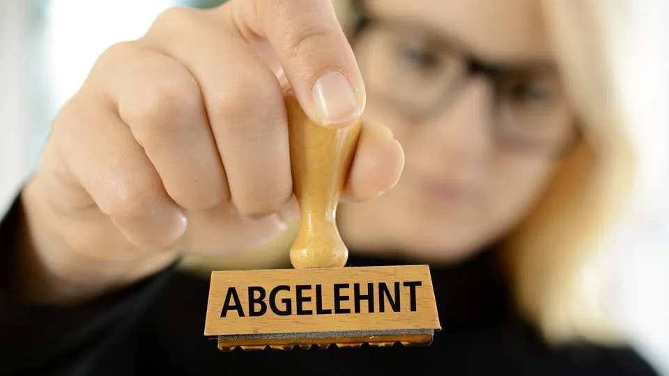 Eine Frau hält einen Stempel mit der Aufschrift "abgelehnt" in der Hand.