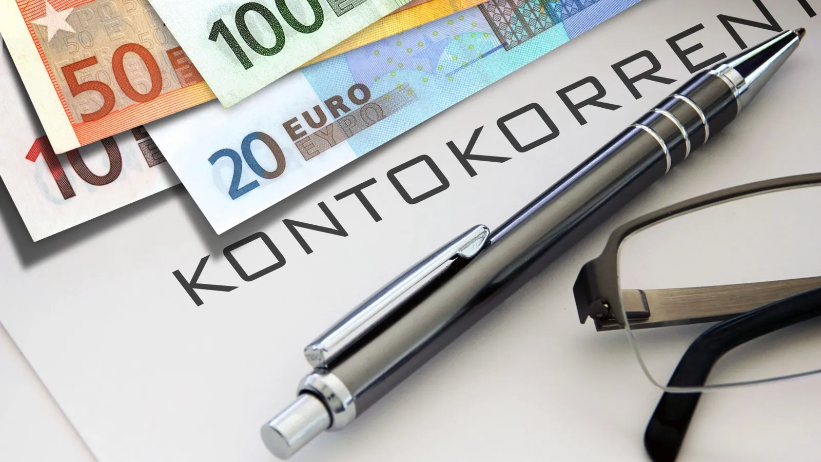 Mehrere Euro-Scheine liegen auf einem Dokument mit der Aufschrift "Kontokorrentkredit", unter dieser Aufschrift liegt ein Kugelschreiber.