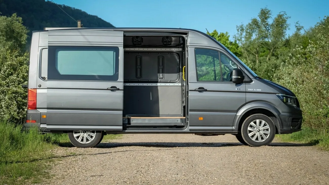 Der graue MAN TGE 3180 4x4 von der Seite mit geöffneter Schiebetür.