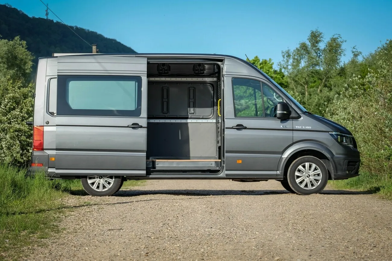 Der graue MAN TGE 3180 4x4 von der Seite mit geöffneter Schiebetür.