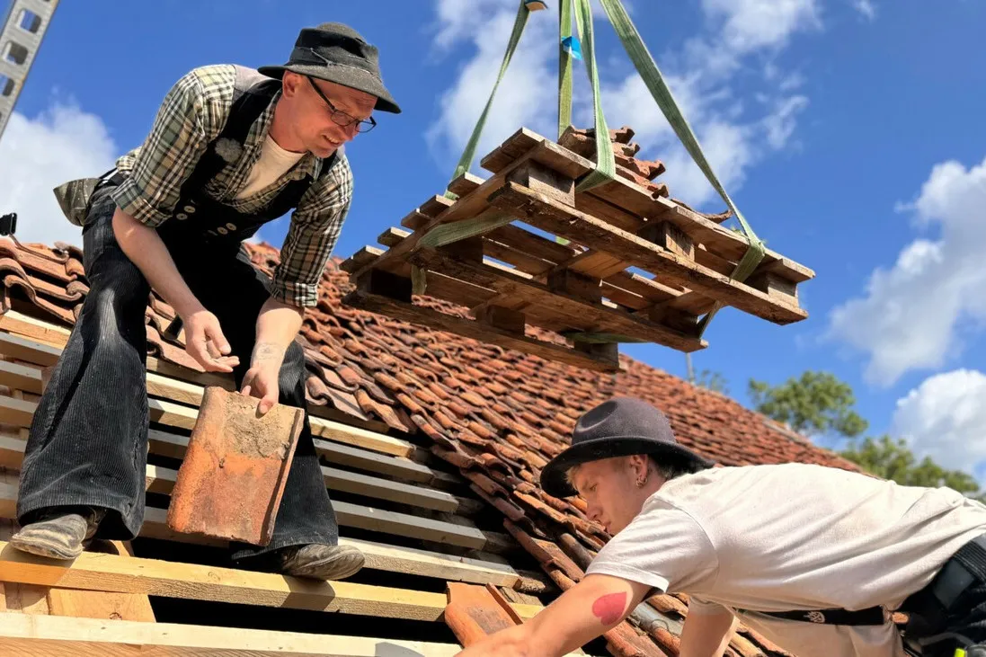 Hier verlegen Azubi und Meister die alten Ziegel wieder fachgerecht auf dem Dach des denkmalgeschützten Hauses.