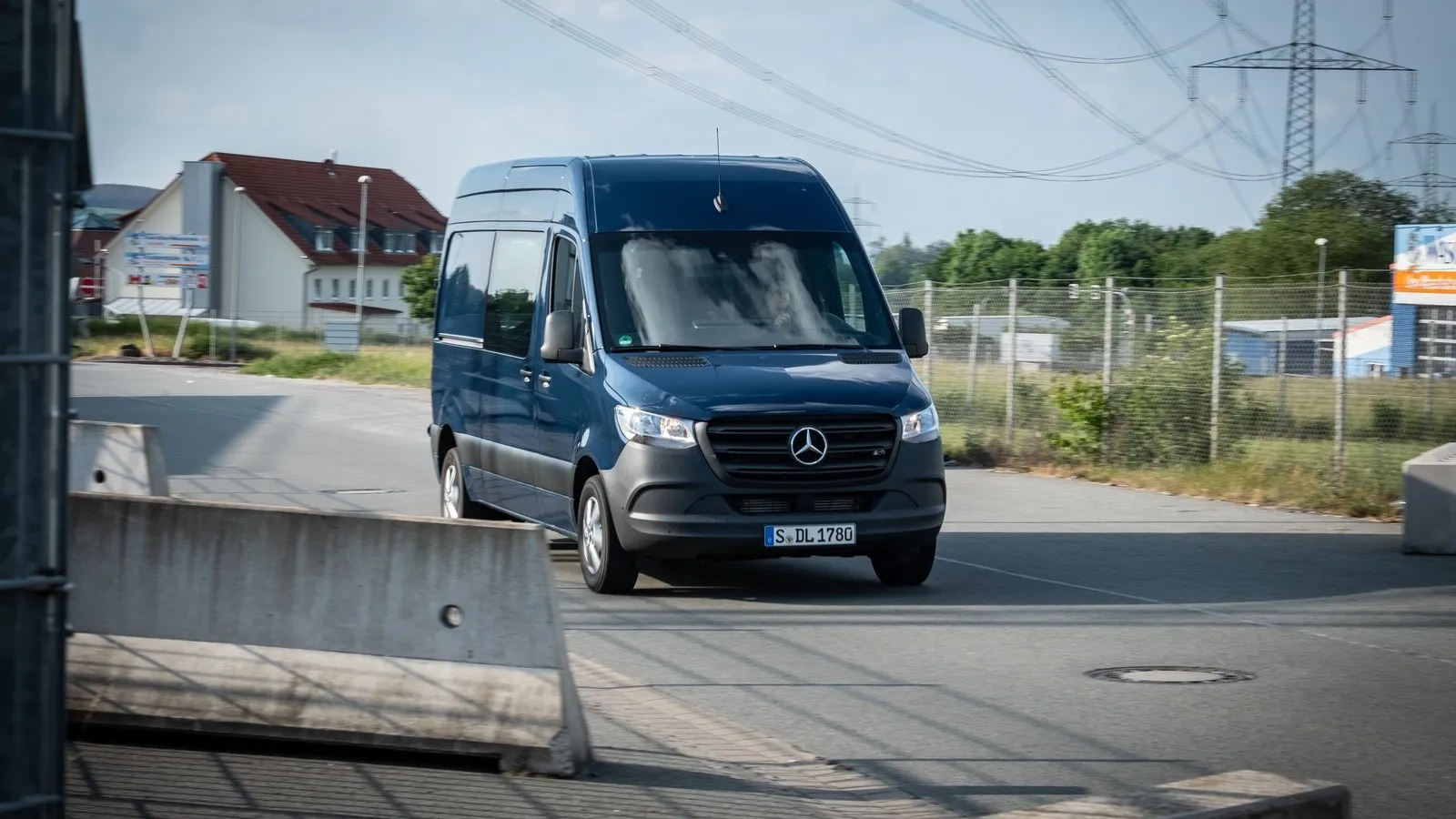 Ein dunkelblauer Mercedes Transporter steht mitten auf einer Straße. Im Hintergrund ist ein Haus und eine Grünfläche zu sehen.