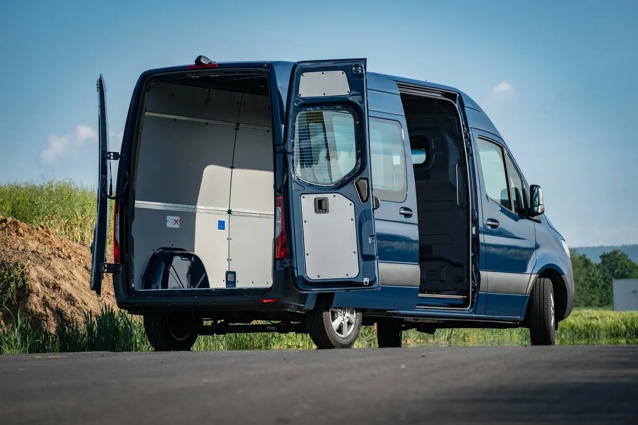 Der dunkelblaue Mercedes Benz Sprinter mit geöffnetem Kofferraum steht auf einer Landstraße.