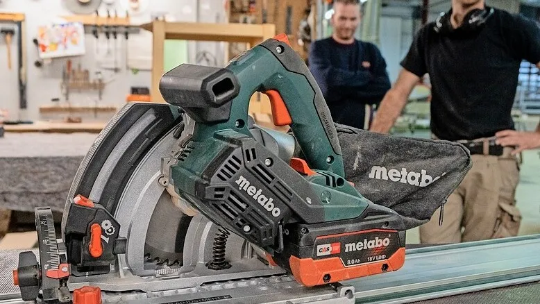 Die neue Metabo Tauchsäge KT 18 LTX 66 BL, dahinter stehen zwei Männer mit schwarzen T-Shirts.