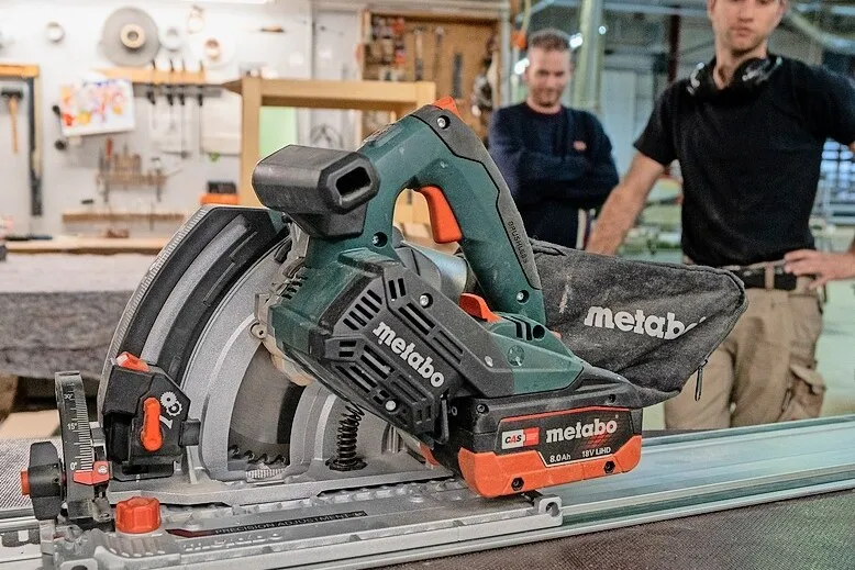 Die neue Metabo Tauchsäge KT 18 LTX 66 BL, dahinter stehen zwei Männer mit schwarzen T-Shirts.