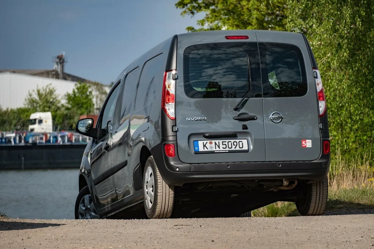 Der grau-schwarze Nissan NV250 von hinten, an einem See stehend.