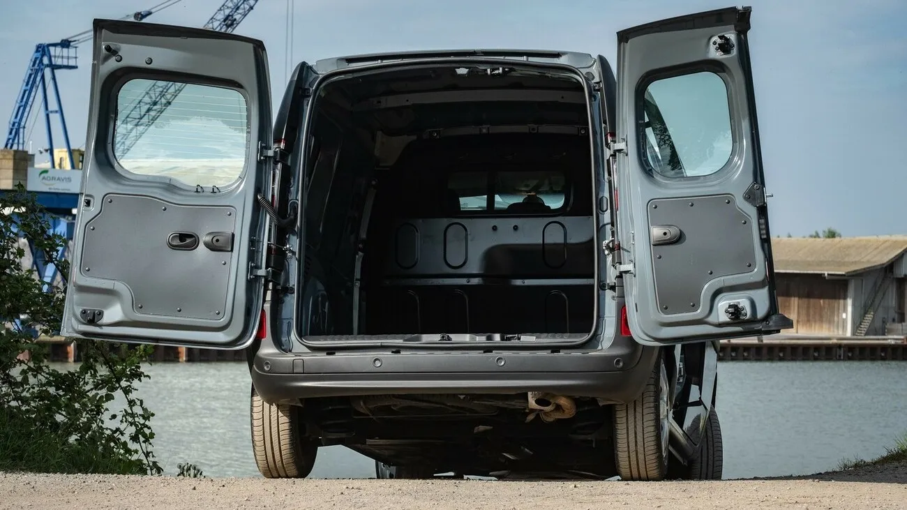 Der grau-schwarze Nissan NV250 an einem See von hinten mit geöffneten Hecktüren.