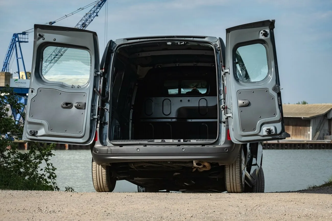 Der grau-schwarze Nissan NV250 an einem See von hinten mit geöffneten Hecktüren.