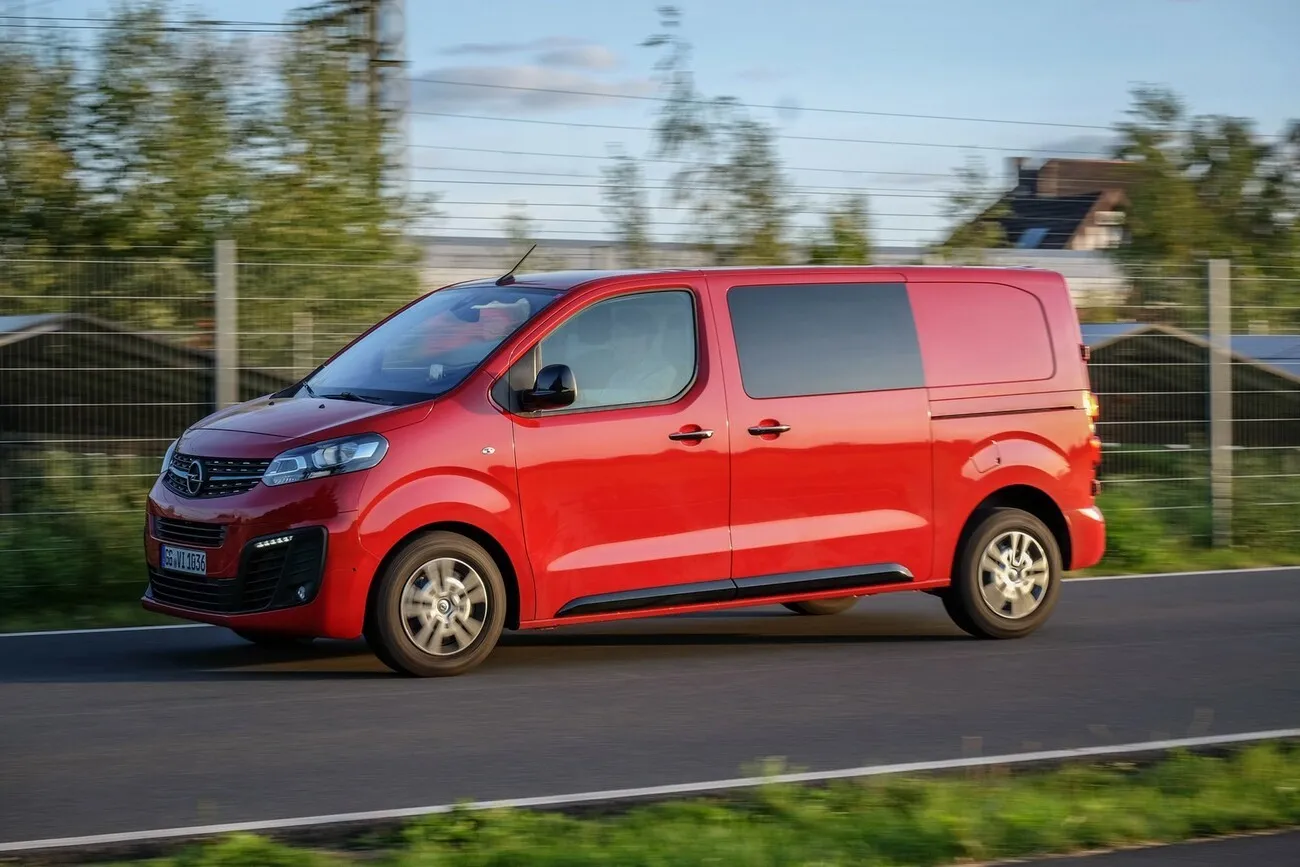 Der rote Opel Vivaro Doka fährt auf einer Straße und ist seitlich zu sehen.