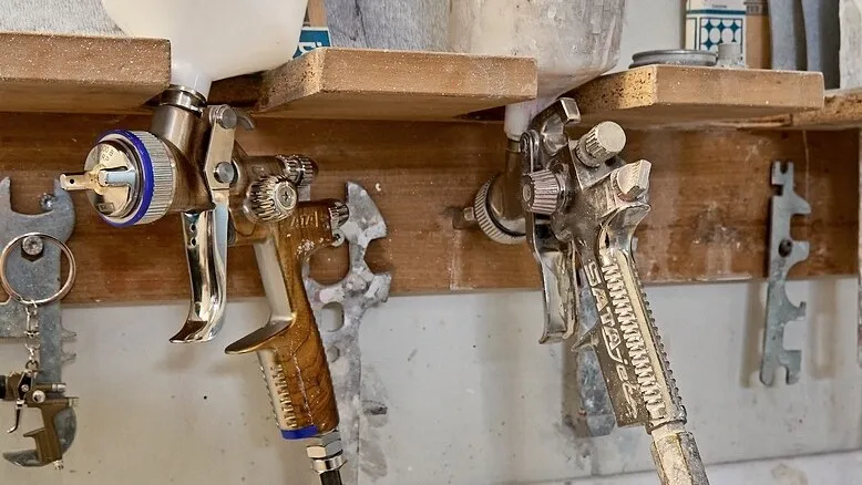 Zwei Lackierpistolen hängen in einer hölzernen Halterung an der Wand.