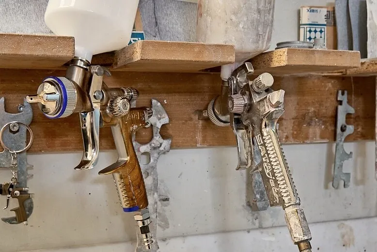 Zwei Lackierpistolen hängen in einer hölzernen Halterung an der Wand.