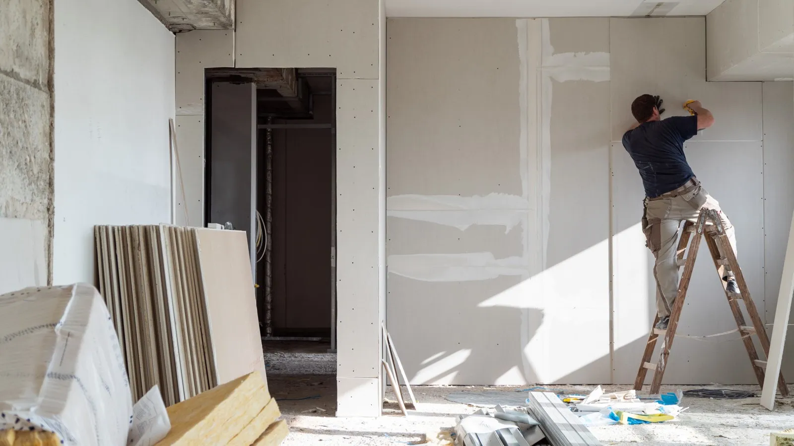 Ein Handwerker arbeitet an einer Wand, in einem Raum im Renovierungszustand.