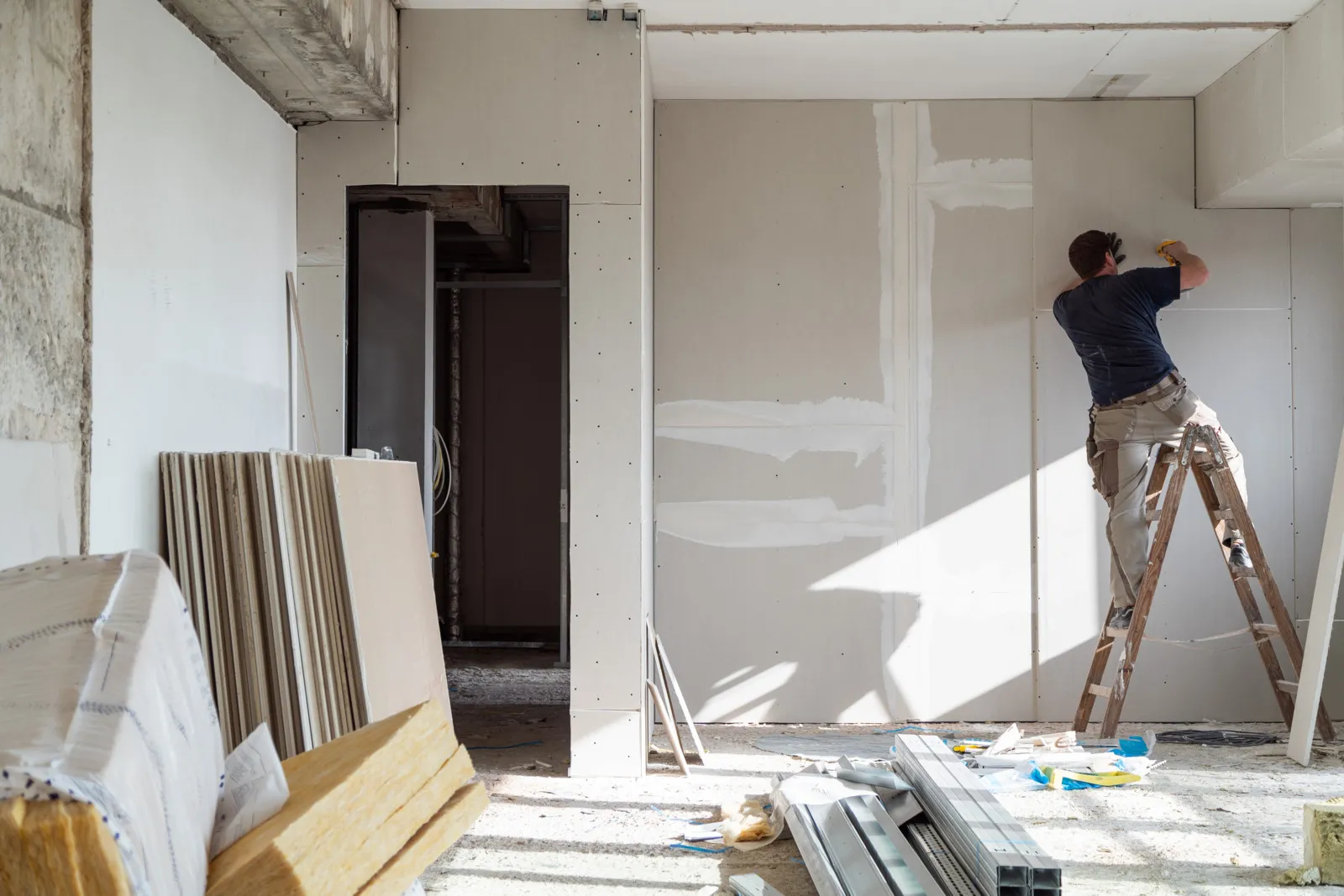 Ein Handwerker arbeitet an einer Wand, in einem Raum im Renovierungszustand.