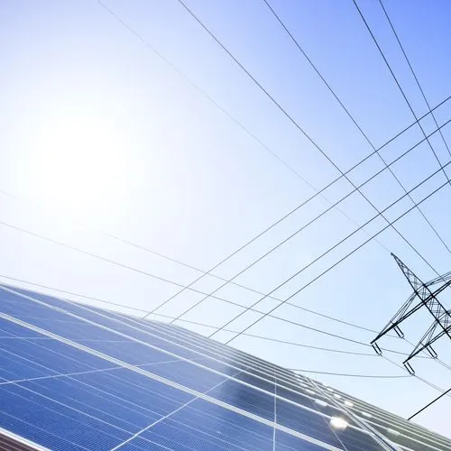 Eine Solaranlage im Vordergrund und ein Strommast im Hintergrund vor blauem Himmel.