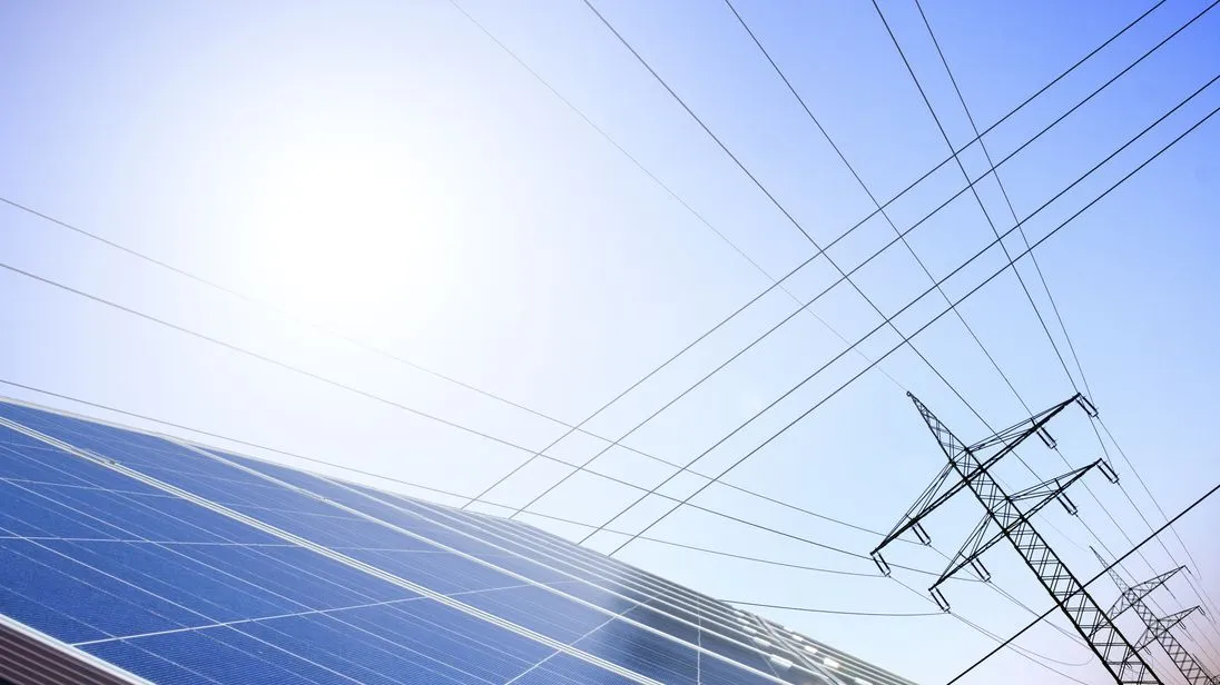 Eine Solaranlage im Vordergrund und ein Strommast im Hintergrund vor blauem Himmel.
