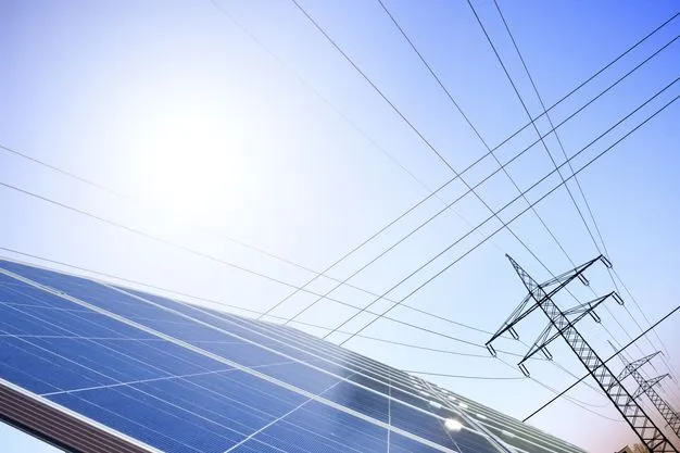 Eine Solaranlage im Vordergrund und ein Strommast im Hintergrund vor blauem Himmel.