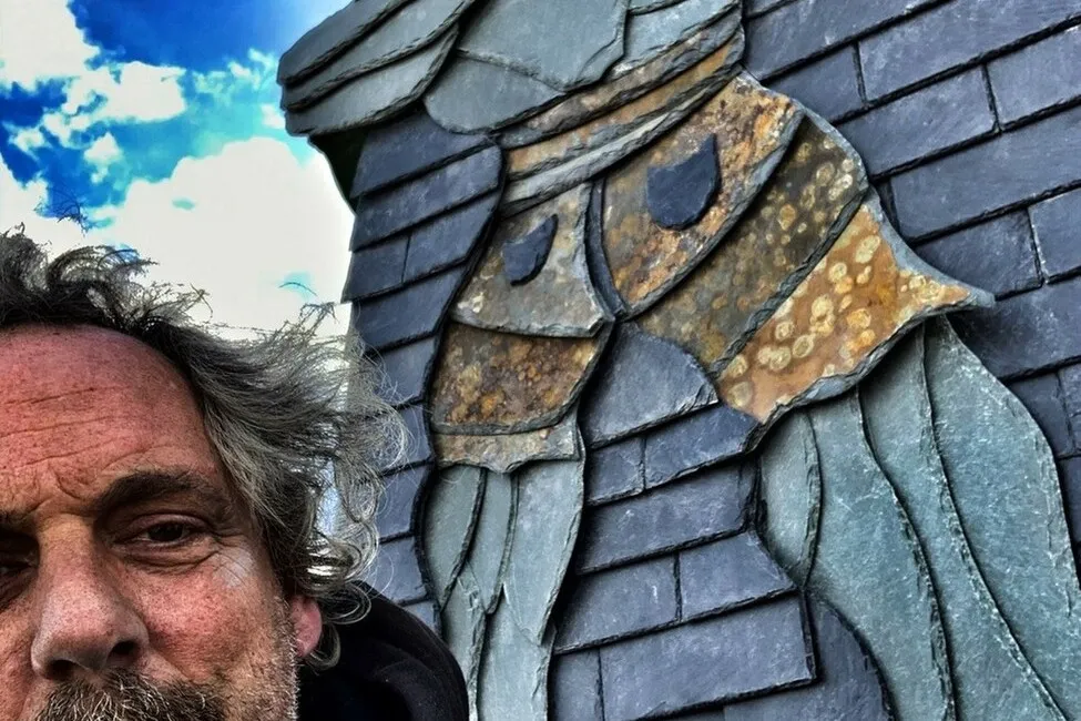 Michael Wenzel steht vor einem Dach, an dem er eins seiner Kunstwerke eingearbeitet hat.