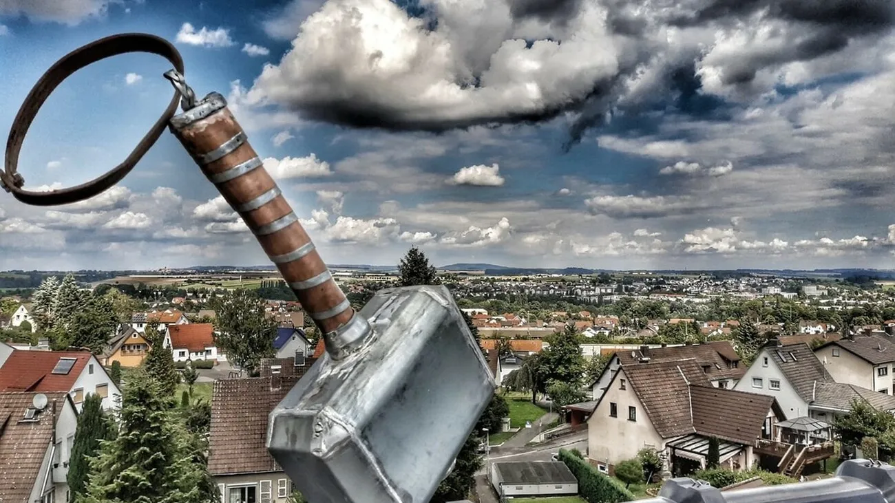 Nahaufnahme eines Daches, Im Fokus steht das Kunstwerk "Thors Hammer" mit vielen Häusern und Bäumen im Hintergrund.