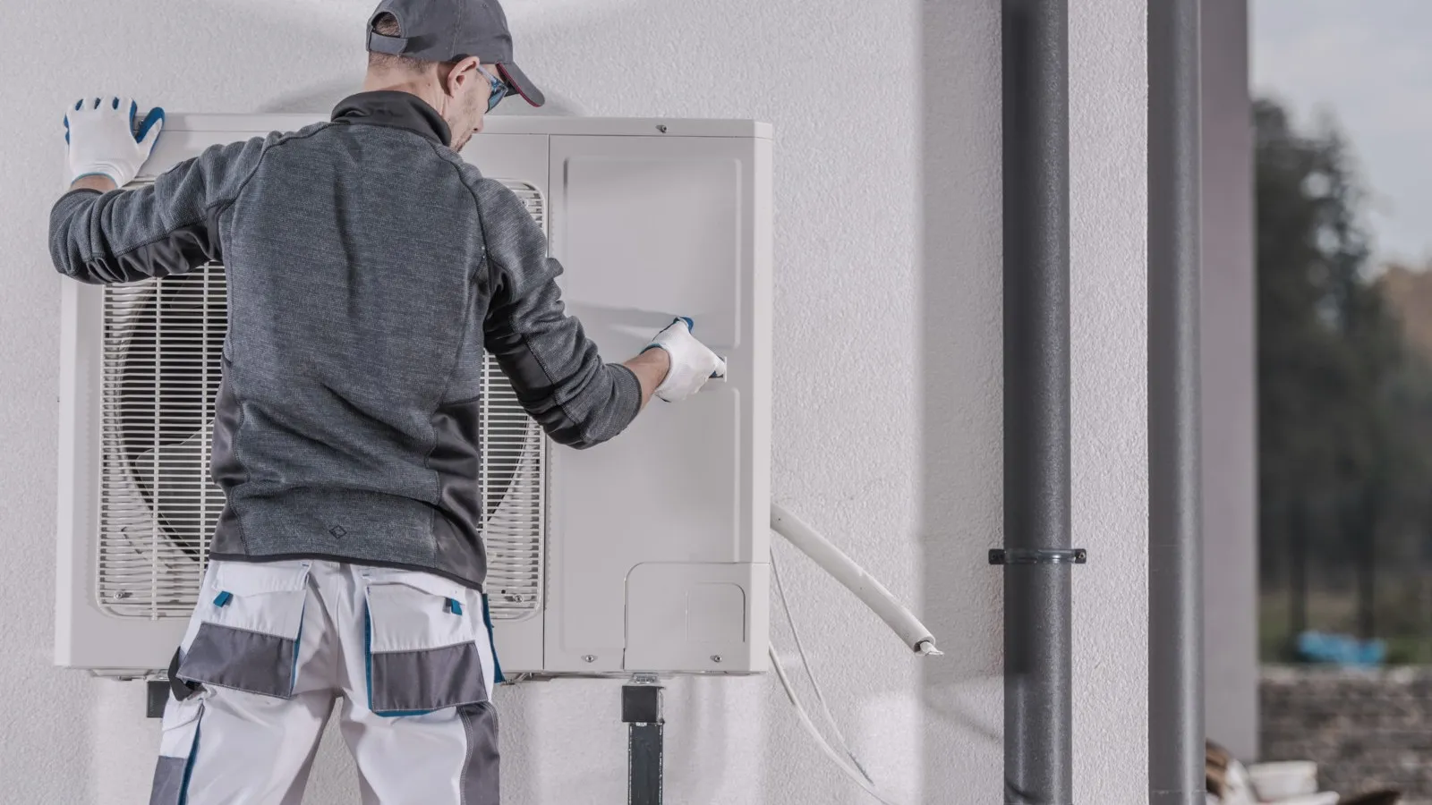 Ein grau gekleideter Handwerker installiert eine Wärmepumpe.