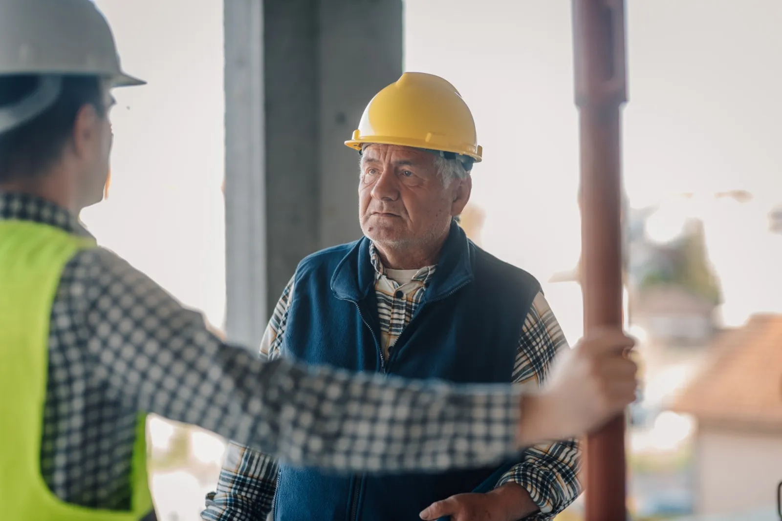 Ein älterer Herr mit gelbem Schutzhelm steht seinem Arbeitgeber gegenüber.