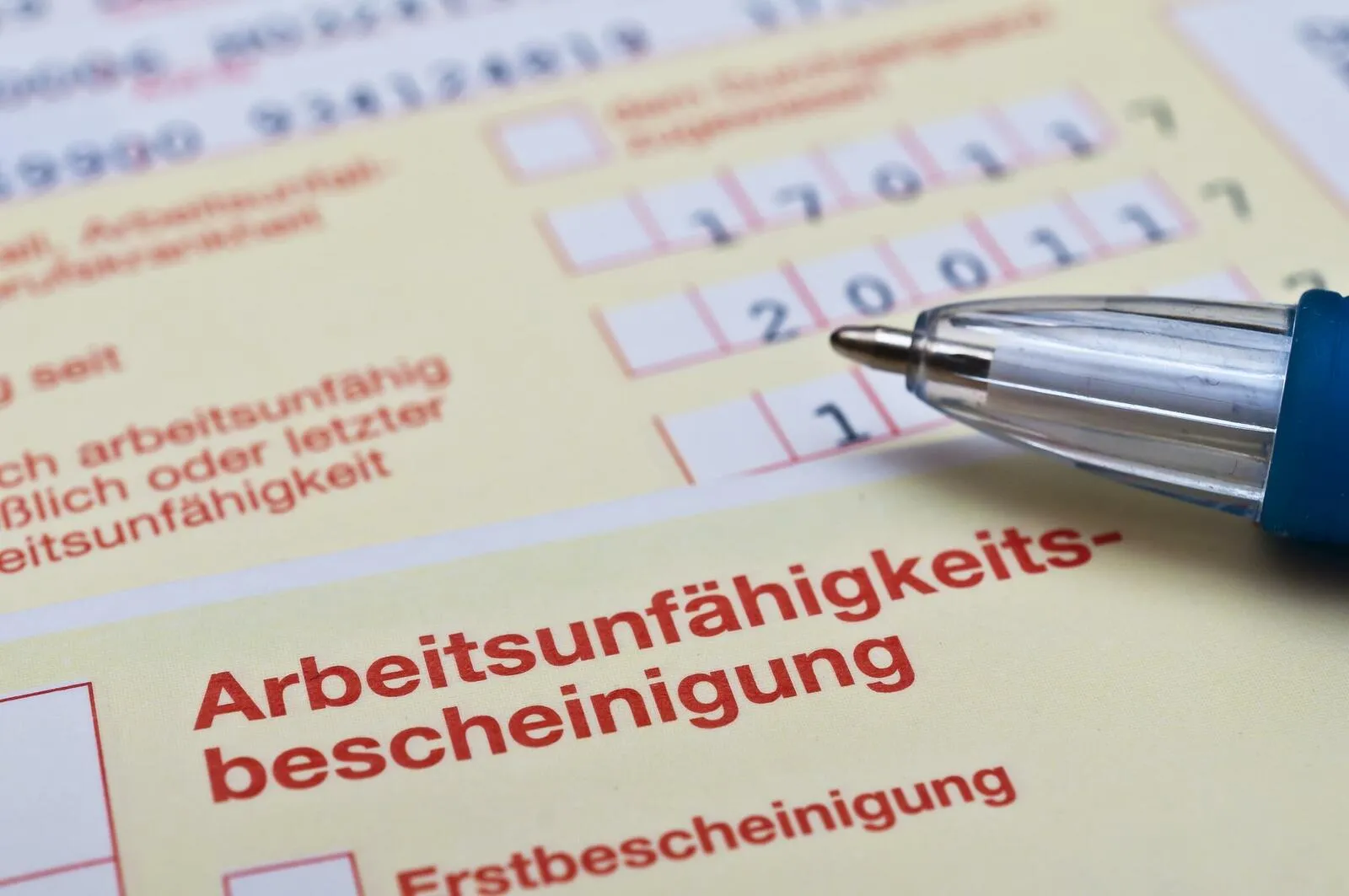 Eine Nahaufnahme einer Arbeitsunfähigkeitsbescheinigung auf der ein Stift liegt, von dem nur das Stiftende zu sehen ist.