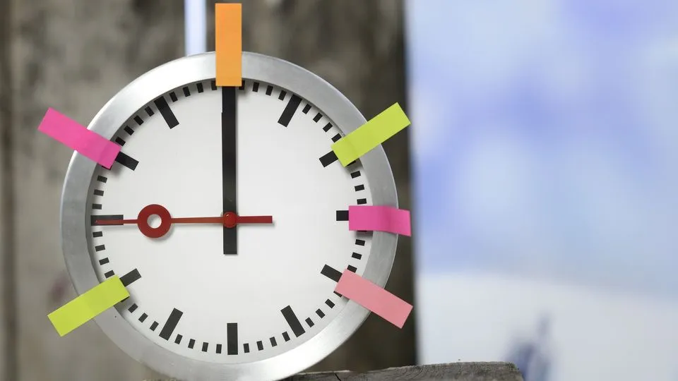 Eine Uhr hängt an der Wand. An der Uhr sind Post-its in verschiedenen Farben angebracht.