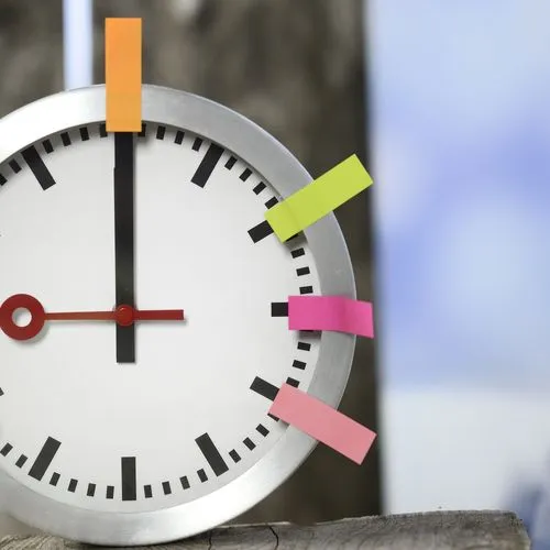 Eine Uhr hängt an der Wand. An der Uhr sind Post-its in verschiedenen Farben angebracht.