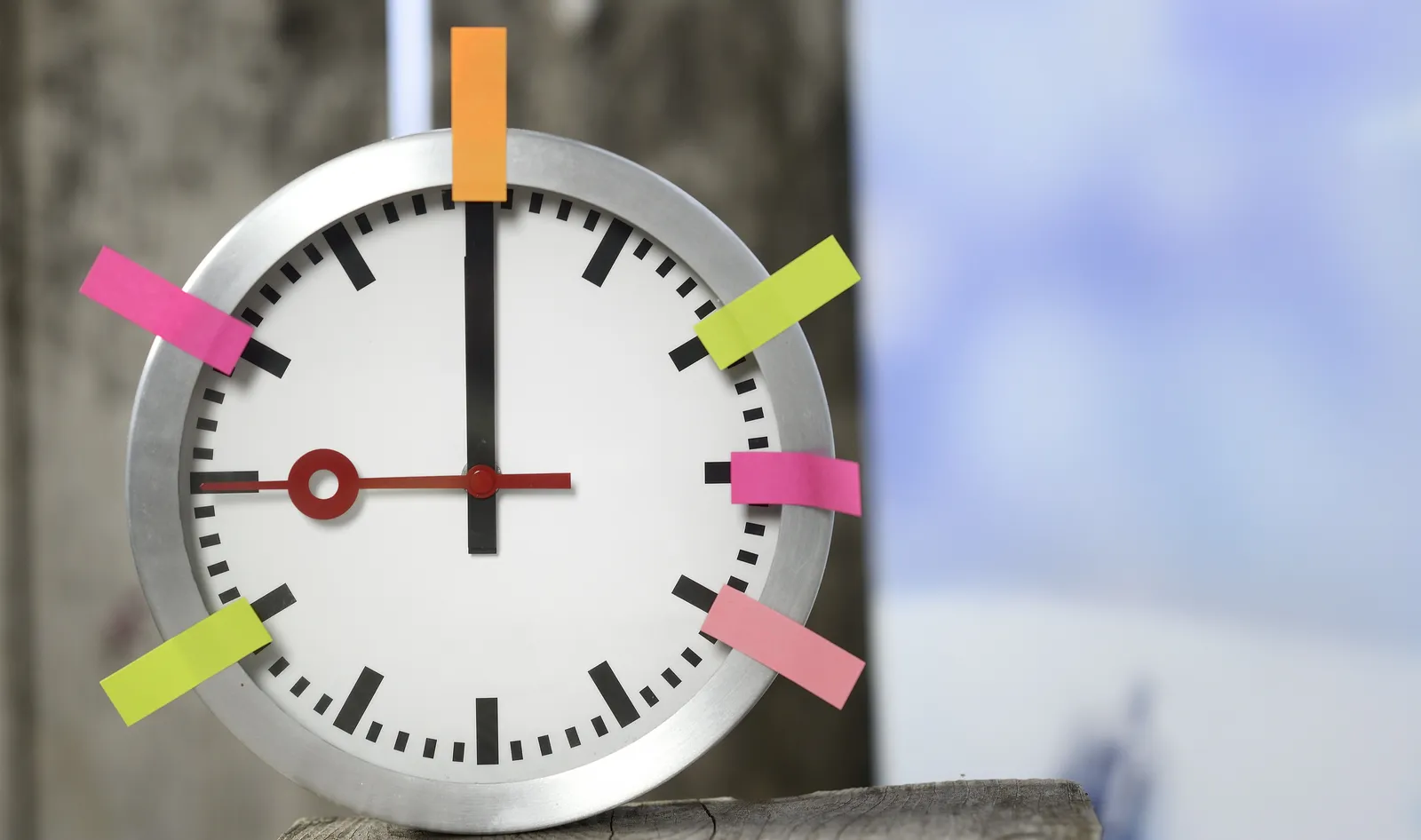 Eine Uhr hängt an der Wand. An der Uhr sind Post-its in verschiedenen Farben angebracht.