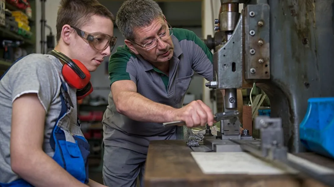 Ausbilder und Azubi im Handwerk an einer Maschine