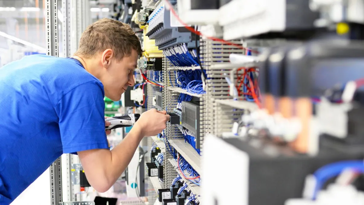 Ein junger Handwerker in einem blauen T-Shirt arbeitet an einem Stromkasten mit blauen Kabeln.