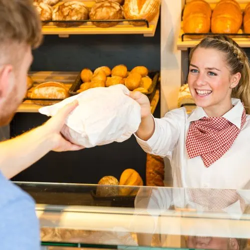 Eine Bäckereiverkäuferin reicht einem Kunden eine Brötchentüte über den Tresen  