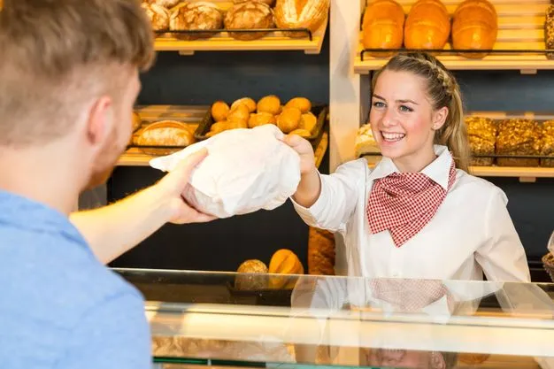 Eine Bäckereiverkäuferin reicht einem Kunden eine Brötchentüte über den Tresen  