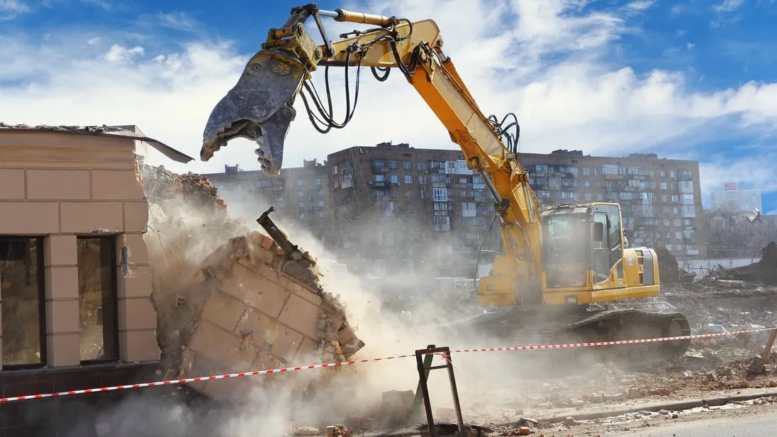 Bagger auf der Baustelle beim Abbruch in einer Staubwolke.