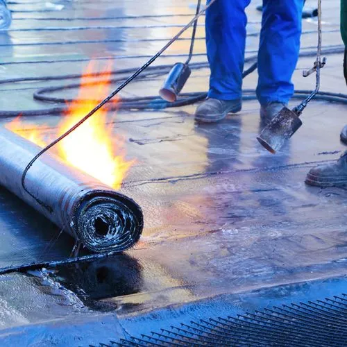 Ein Dachdecker dichtet ein Fachdach mit Bitumen ab.