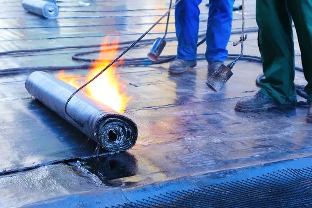 Ein Dachdecker dichtet ein Fachdach mit Bitumen ab.