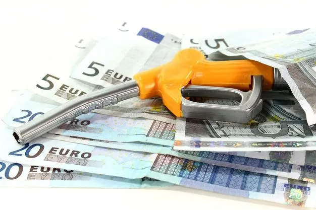 Mehrere 5 und 20 Euro Scheine liegen halb aufeinander, darauf liegt sich eine Zapfpistole.