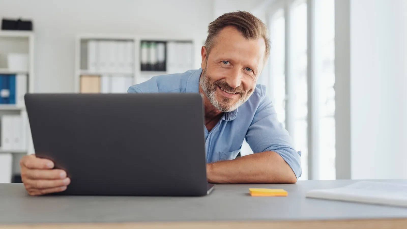 Ein Mann sitzt an einem Laptop und lächelt ins Bild.