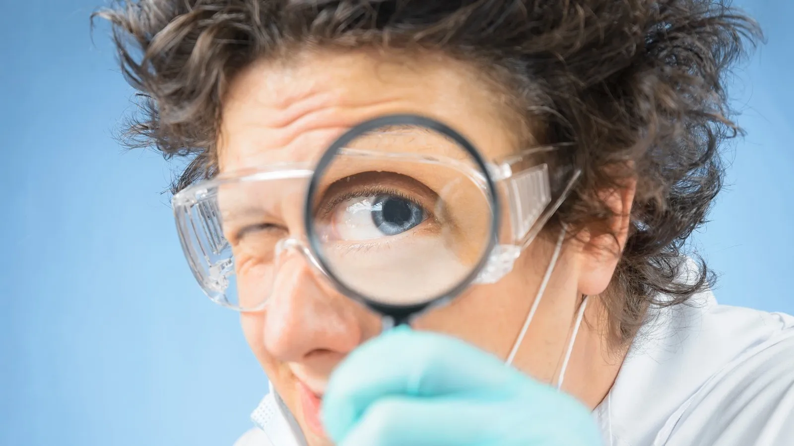 Verrückter Professor hält sich eine Lupe vor das Auge.