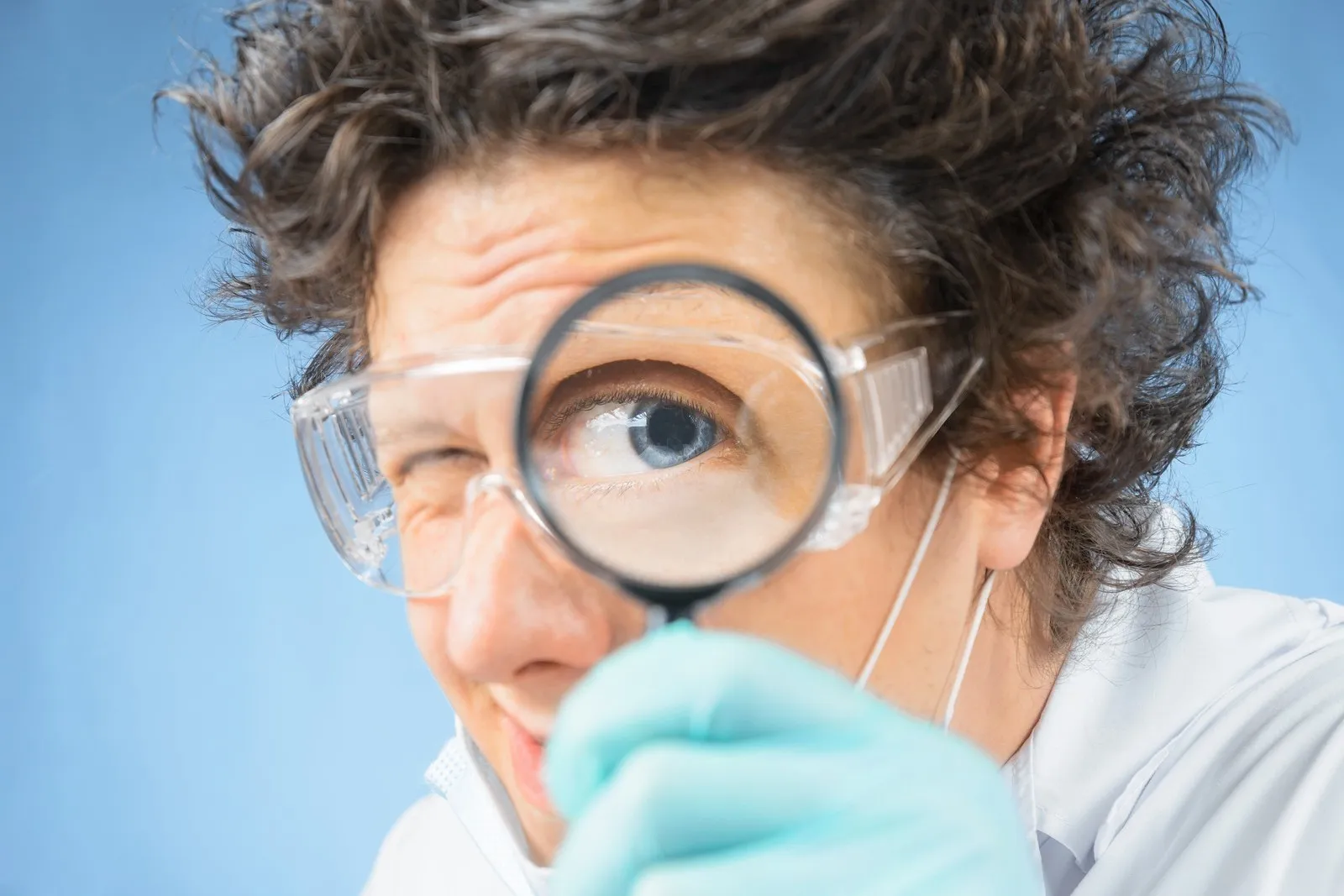 Verrückter Professor hält sich eine Lupe vor das Auge.