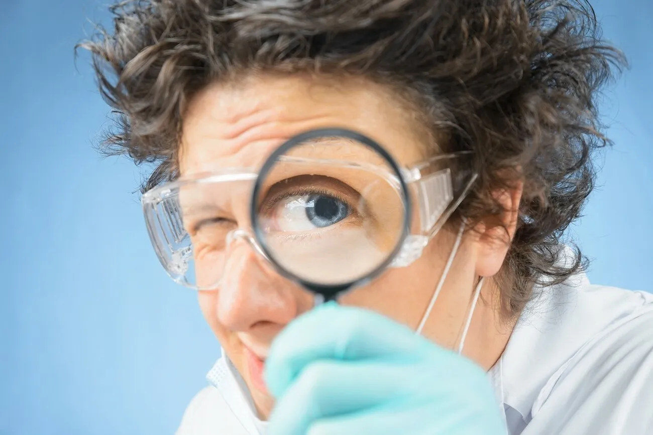 Verrückter Professor hält sich eine Lupe vor das Auge.