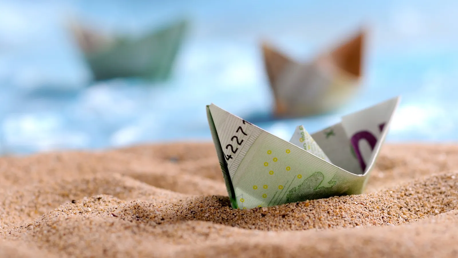 Ein Boot aus einem gefalteten 100-Euro-Schein im Sand.